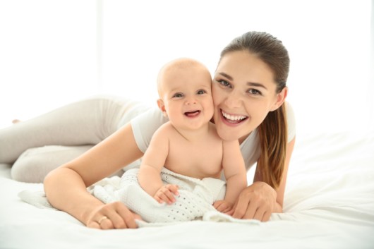 A happy mommy and a baby smiling and lying on the bed