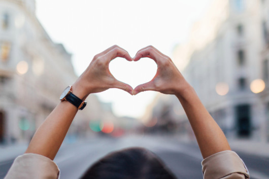 A girl put her arms in the air and holds her fingers in the shape of heart