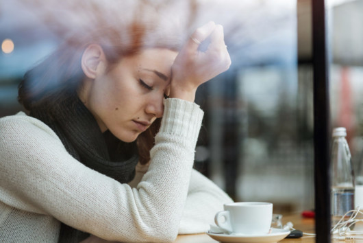 Girl in white sweater sitting in the cafe with a headache.