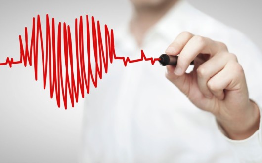 A doctor is drawing a red heart with a pen in front of him