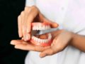 A doctor on black background is holding denture in her hands