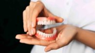 A doctor on black background is holding denture in her hands