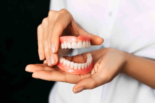 A doctor on black background is holding denture in her hands