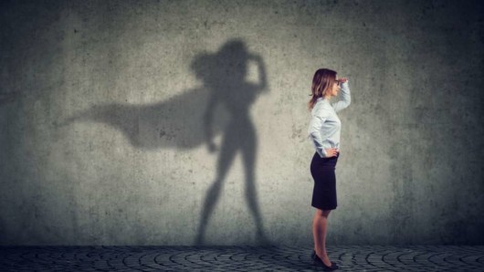 A woman is standing in front of the wall feeling non confident and her with her shadow as a wonder woman 