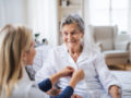 A health care nurse is helping the old lady to dress at home