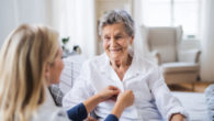 A health care nurse is helping the old lady to dress at home