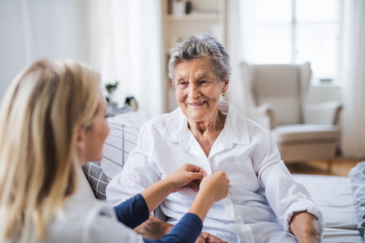 A health care nurse is helping the old lady to dress at home