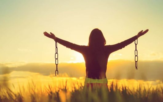 A young girl is staying with her arms spread to the sites welcoming the sunrise