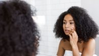 A young and beautiful girl looking in to the mirror and checking her skin for wrinkles