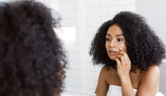 A young and beautiful girl looking in to the mirror and checking her skin for wrinkles