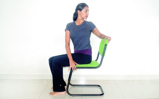 Girl is sitting on the chair and doing chair rotations exercise for back