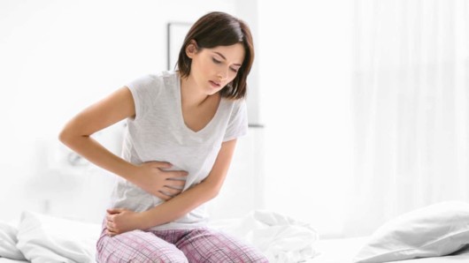 Woman with stomachache or gastric pain sitting on the sofa and suffering with pain