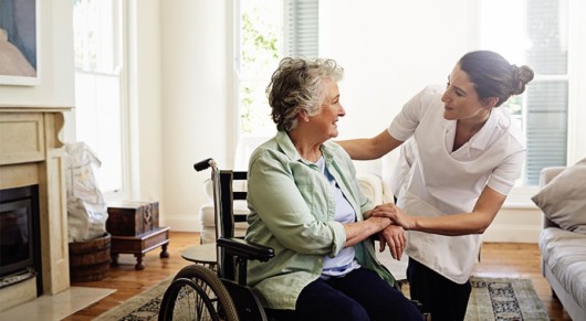 A home nurse is talking to a woman on the wheelchair. They are smiling 