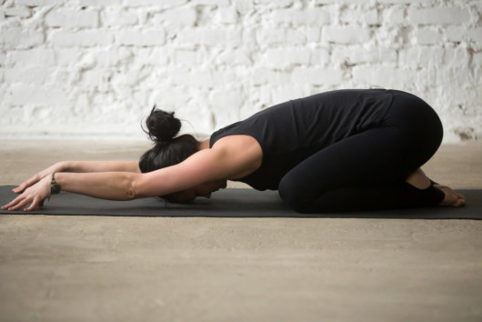 Girl is lying on the floor in a child's pose to ease the back pain