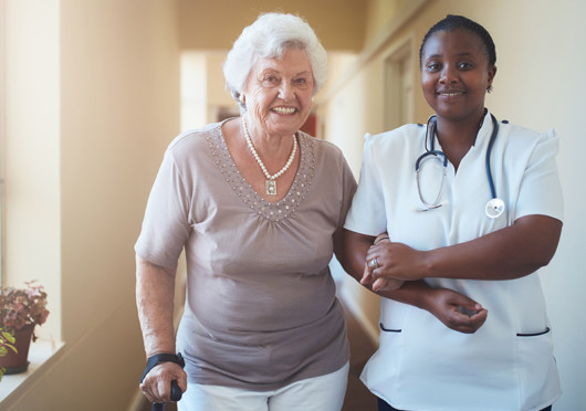 A home nurse is helping the old lady to walk. They are both smiling