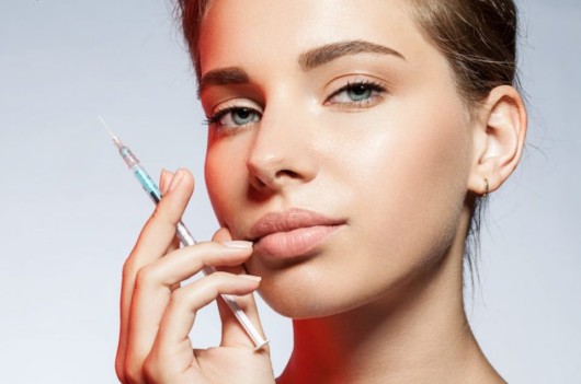 A young looking girl with ideal skin is holding a syringe with botox