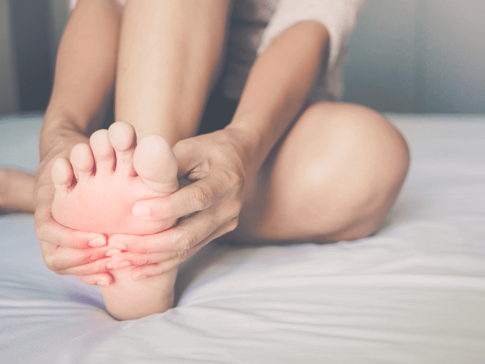 Girl is sitting on the bed and holding her foot with gout