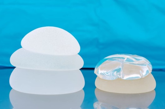 Different types of breast implants are on the table against a blue background