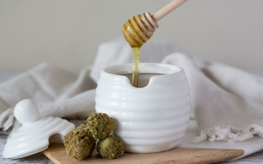 Honey in the white jar with hemp flowers next to it