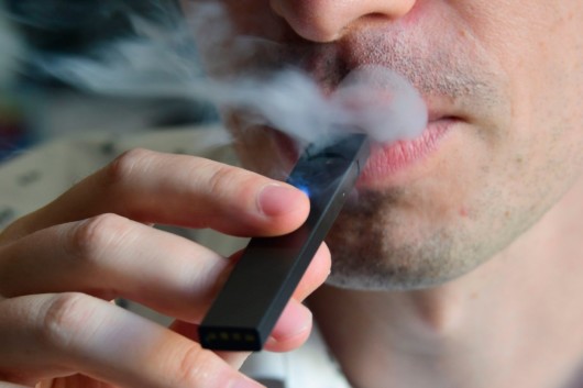 A close up face of a guy who is vaping 