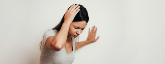 Girl with dizziness is holding her head and leaning against white the wall