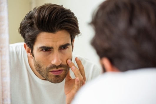 Young man is checking his face for wrinkles or age changes in front of the mirror 