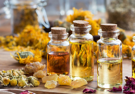 Three transparent bottles filled with essential oils are on the table with dry yellow flowers and natural pieces of salt around