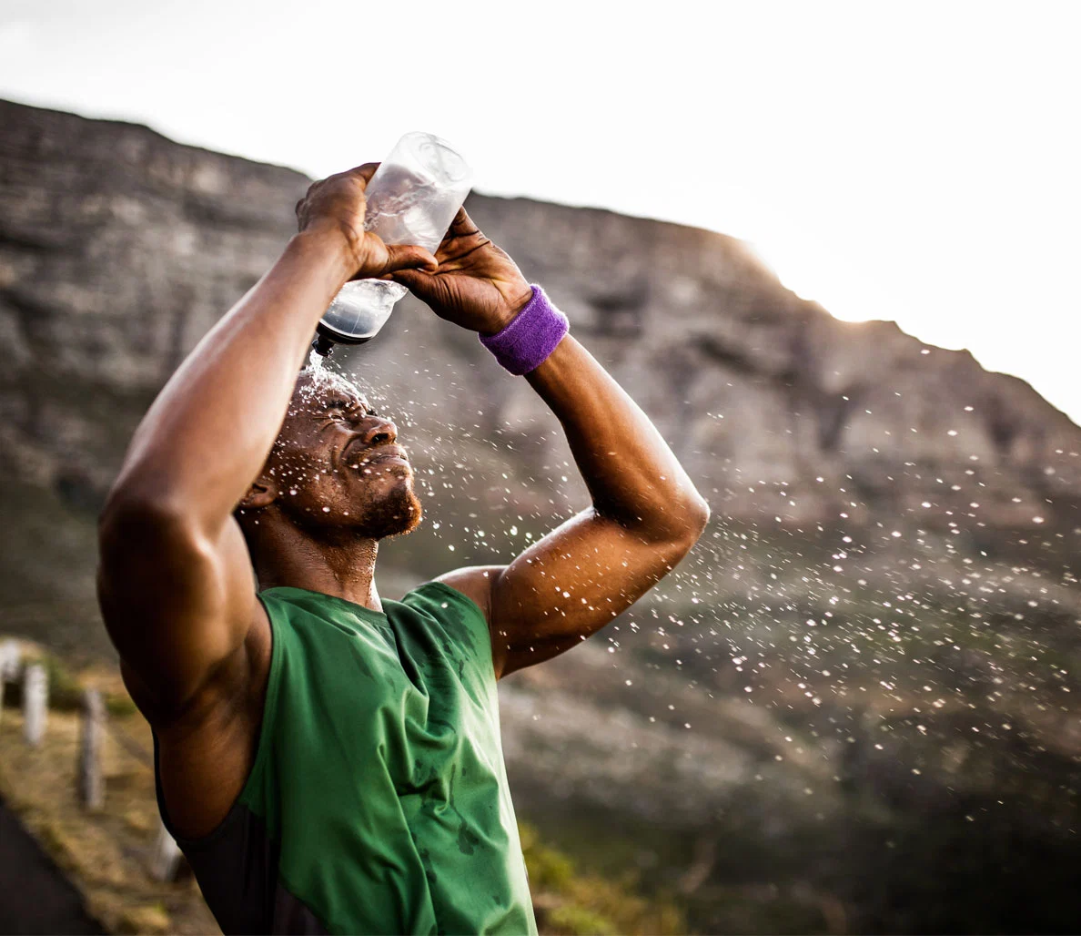 A guy is pouring water on himself after exercising in the sun