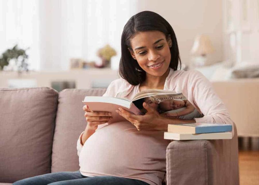 A pregnant woman is reading a book about pregnancy and the baby