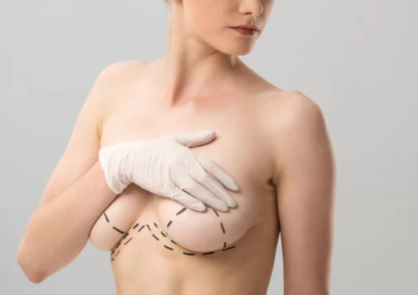 A torso of a young girl on grey who is covering her breasts with a hand