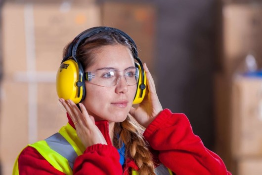 A young lady is wearing yellow headphones to protect her ear from loud noise at work