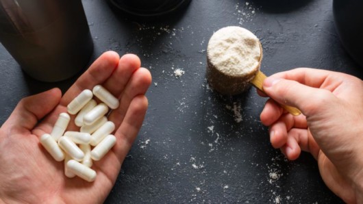 the guy is holding protein powder in a measure cup and pills in his palms