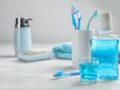Tooth brushes, floss, mouth wash, soap and a towel are on the table against grey background
