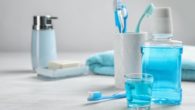 Tooth brushes, floss, mouth wash, soap and a towel are on the table against grey background