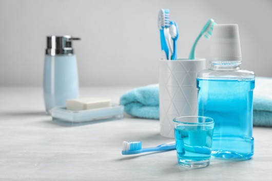 Tooth brushes, floss, mouth wash, soap and a towel are on the table against grey background