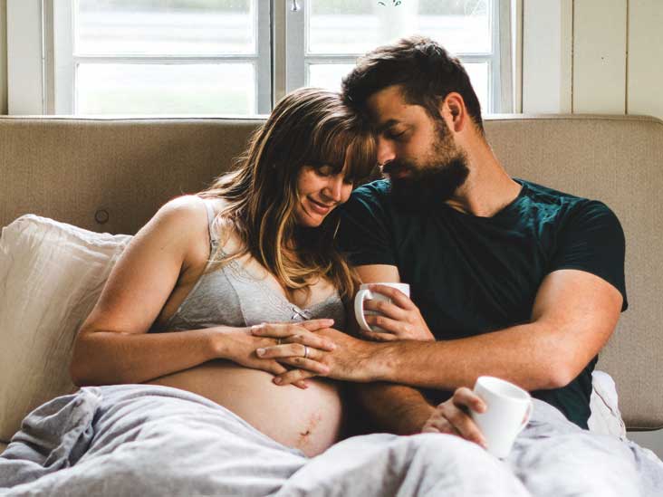 A pregnant woman and her man are sitting next to each other on the sofa