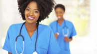 A black woman dressed as a medical assistant in blue outfit is smiling into the camera