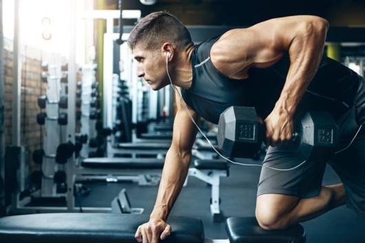 A strong and physically developed guy is exercising in the gym with a dumbbell