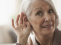 An elderly woman is trying to listen with cupping her ear