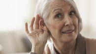 An elderly woman is trying to listen with cupping her ear