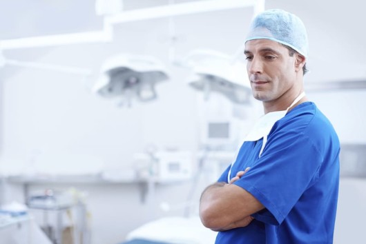 A plastic surgeon is standing in the operating room in the blue gown