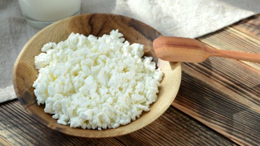 Cottage cheese in a wooden plate on the wooden background