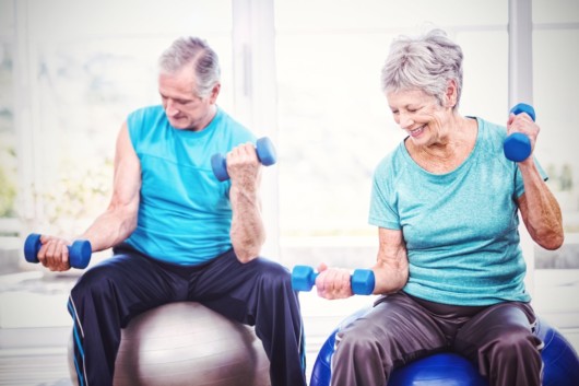 Senior people are doing exercises on the fitness balls with dumbbells