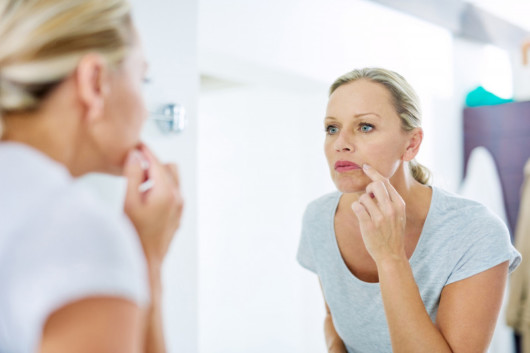 The woman is checking her skin in the mirror for cancer signs