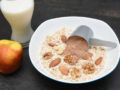 A plate of fry oatmeal with nuts and scoop of chocolate protein on the dark background with a glass of milk and an apple