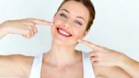 A young girl on white background is smiling and pointing at her white teeth