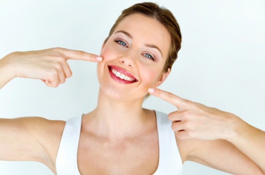 A young girl on white background is smiling and pointing at her white teeth