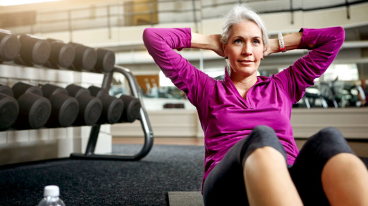 A senior lady is doing crunches in the gym