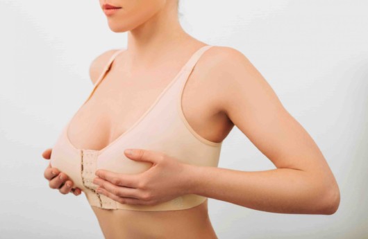 A woman in post surgical bra is holding her augmented breast on the white