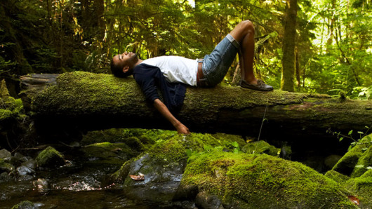 The guy is lying and relaxing on the tree trunk in the forest